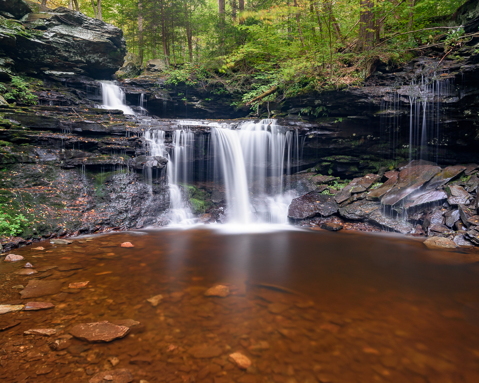 Water flows over the edge of a shelf and into a rust-colored pool.