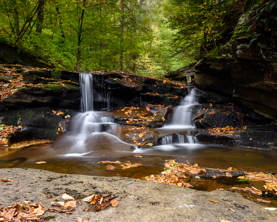 Autumn leaves linger on the rocks around a waterfall.