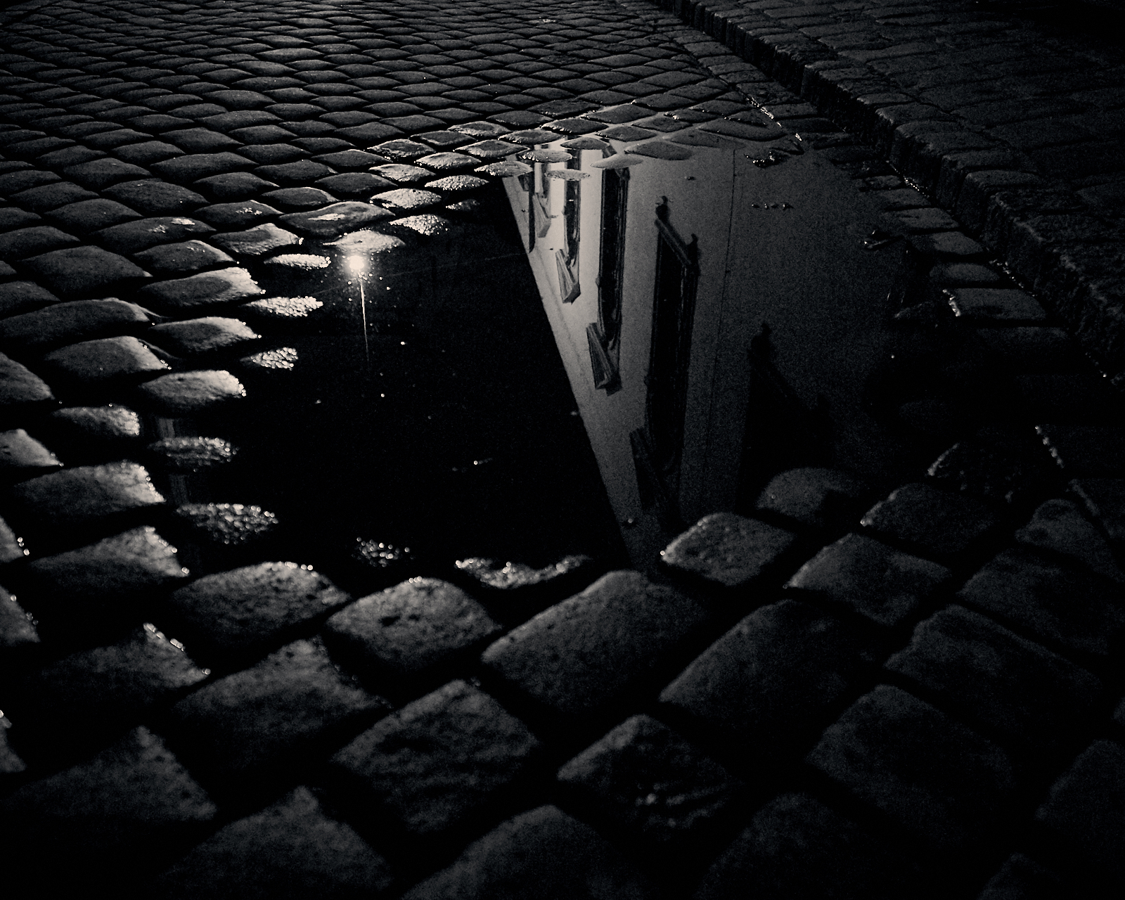 A puddle reflects a streetlight late at night.