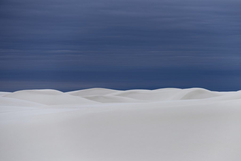 Otherworldly white dunes under a blue overcast sky.