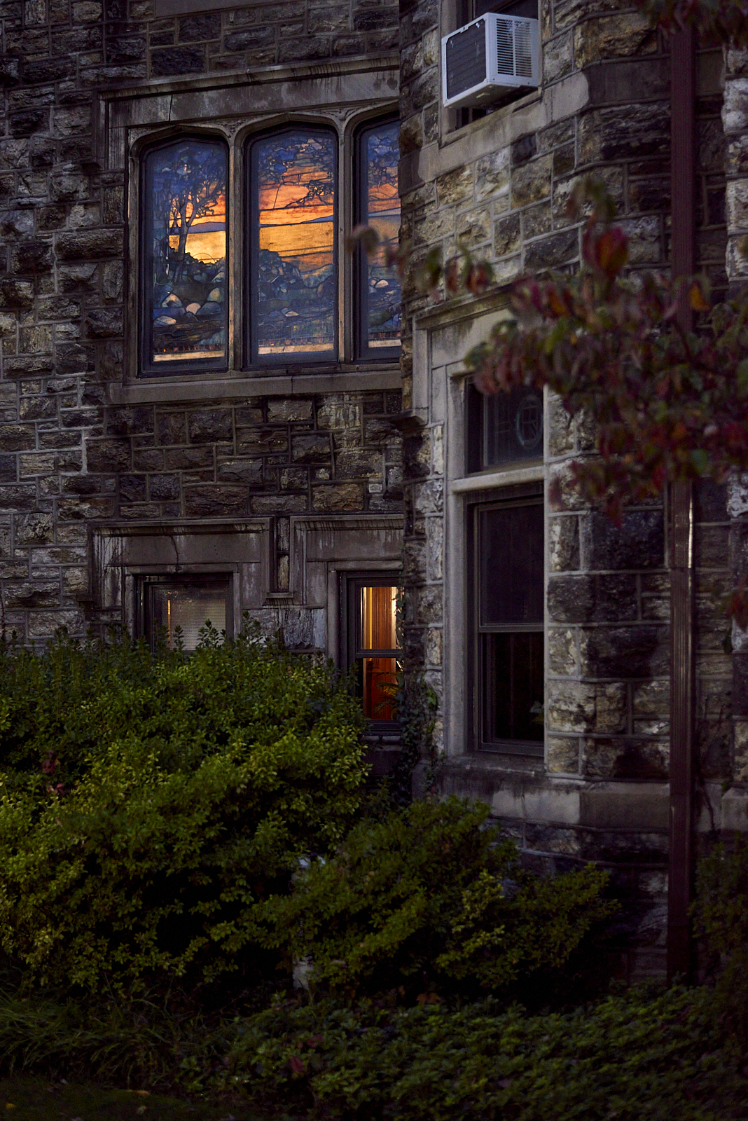 Urban #221017.1 A color photograph of the side of a former estate, Tiffany windows glowing orange.