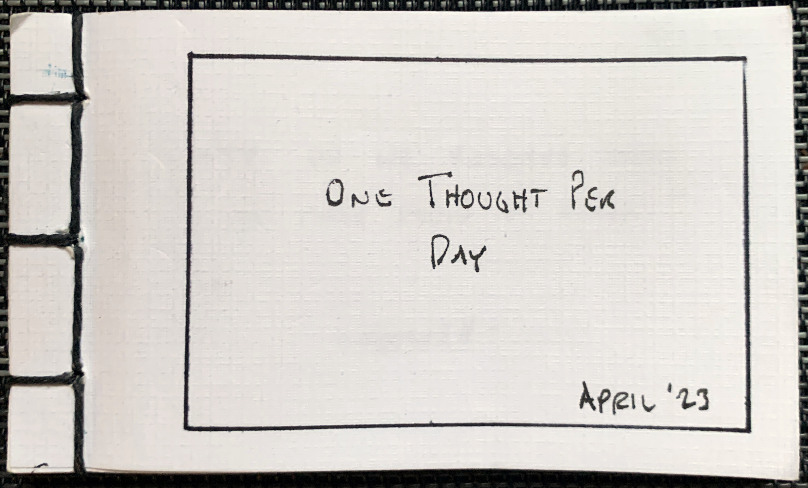 The cover of a little book I made, in which I record one thought each day. The title, written across the cover, is: One Thought Per Day. April ’23.