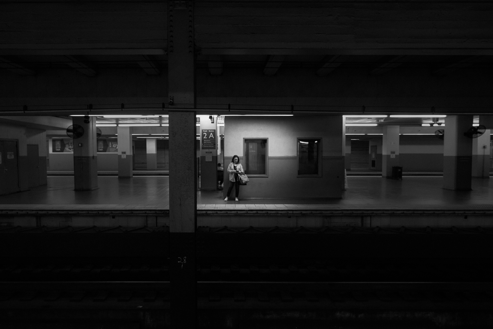 Urban #230421. A woman alone on a darkened subway platform staring at her phone.