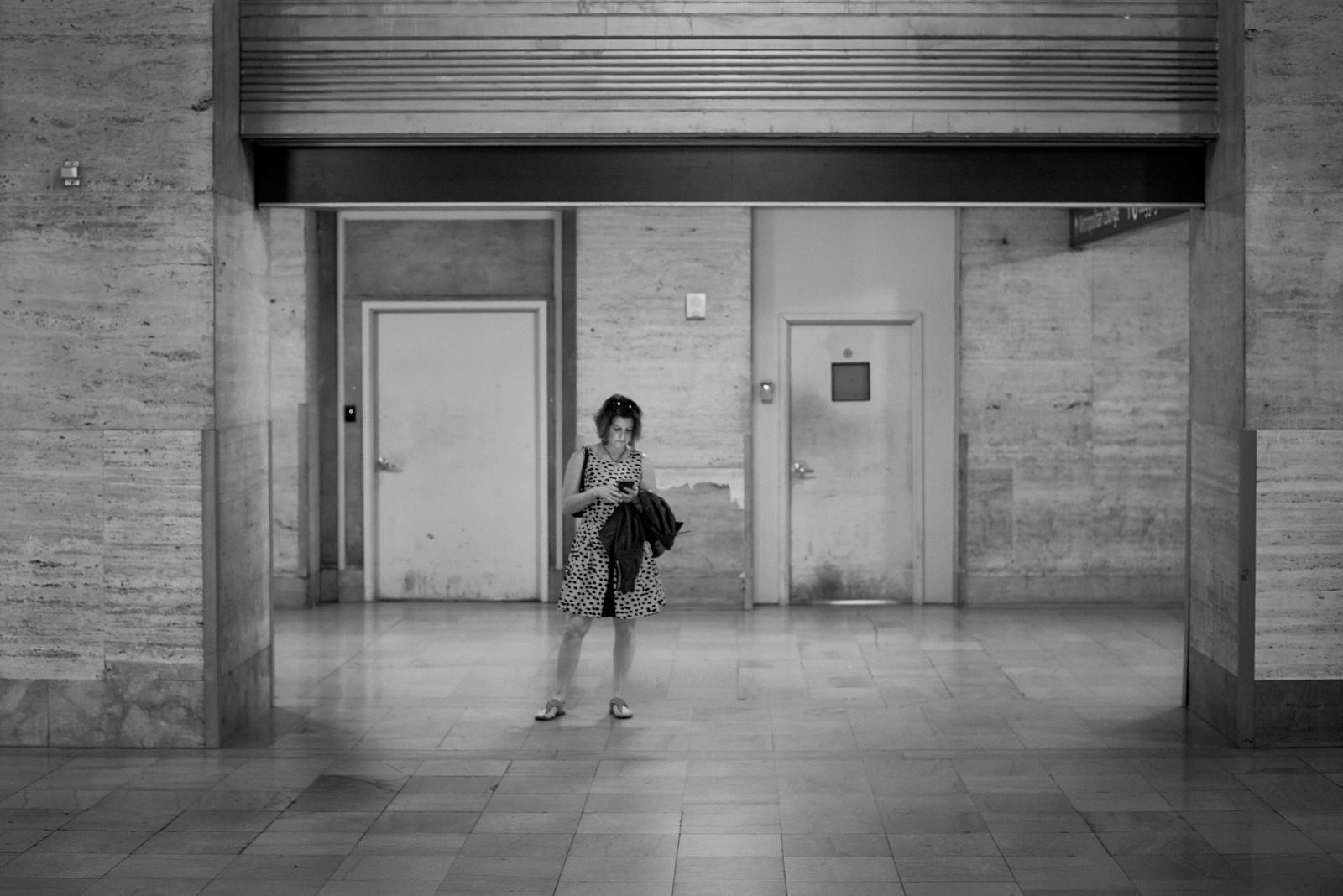 Urban #230510.0. A black and white photograph of a woman standing in 30th Street Train Station looking at her phone.