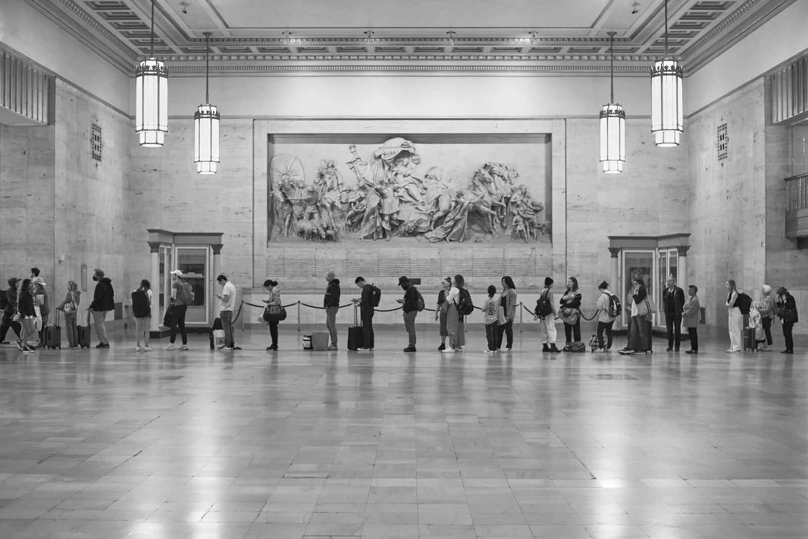 Urban #230510.1. A black and white photograph of a line of people in 30th Street Train Station waiting to board a train.