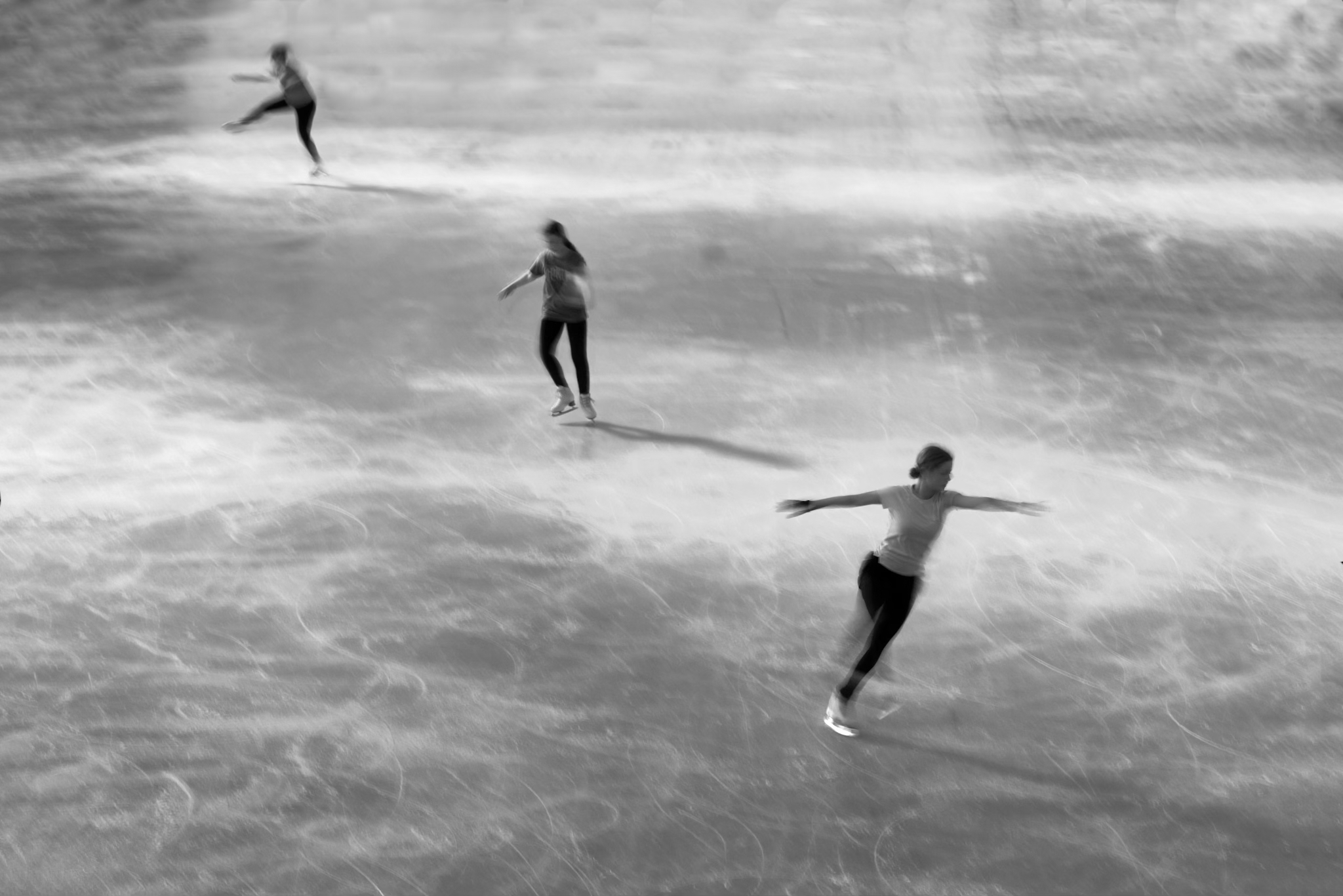 Urban #230721. A black and white photograph of three people ice skating. The skaters are all in motion.