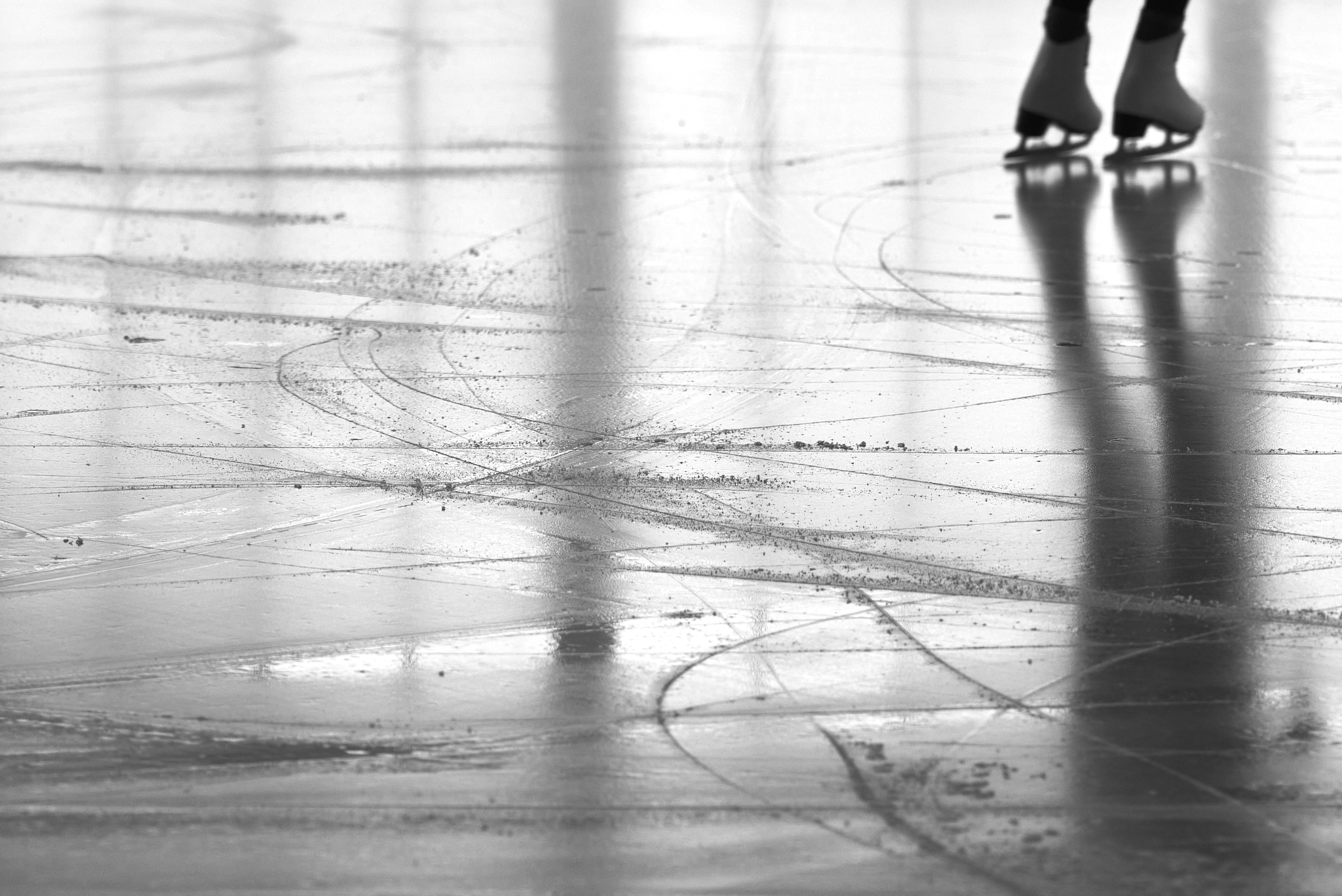 Urban #230727.2. Black and white photograph of a person ice skating away, showing just the skates on the ice.