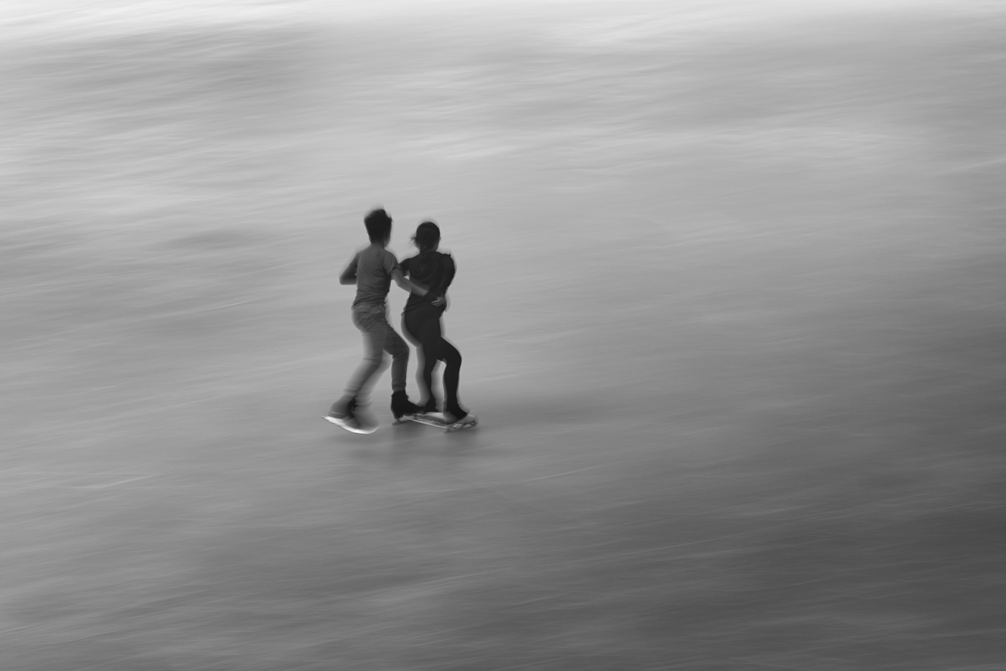 Urban #230718. A black and white photograph, slightly blurred, of two people ice skating.