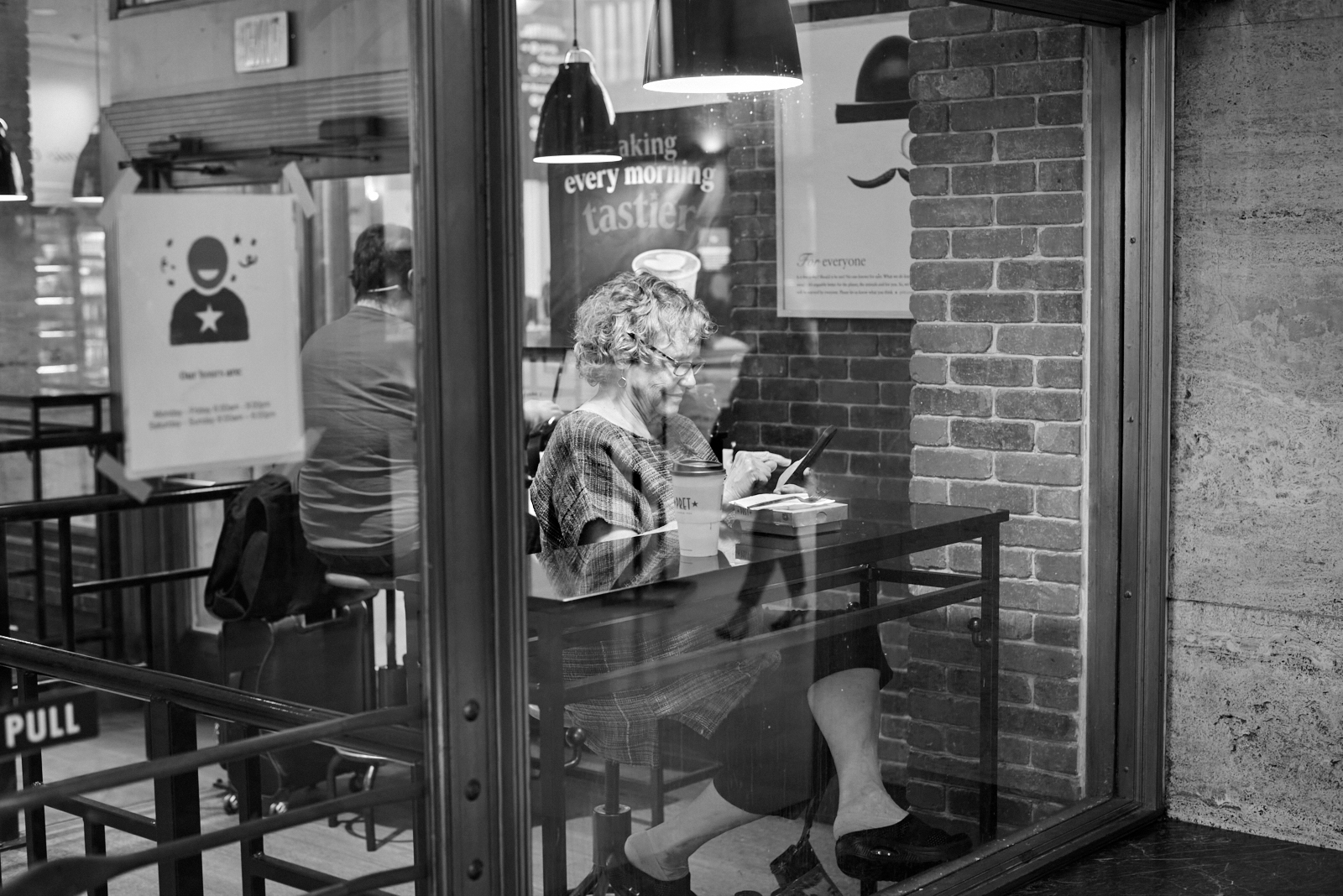 Urban #230510.3. A black and white photo of a woman sitting in Pret à Manger in 30th Street Station looking at her phone.