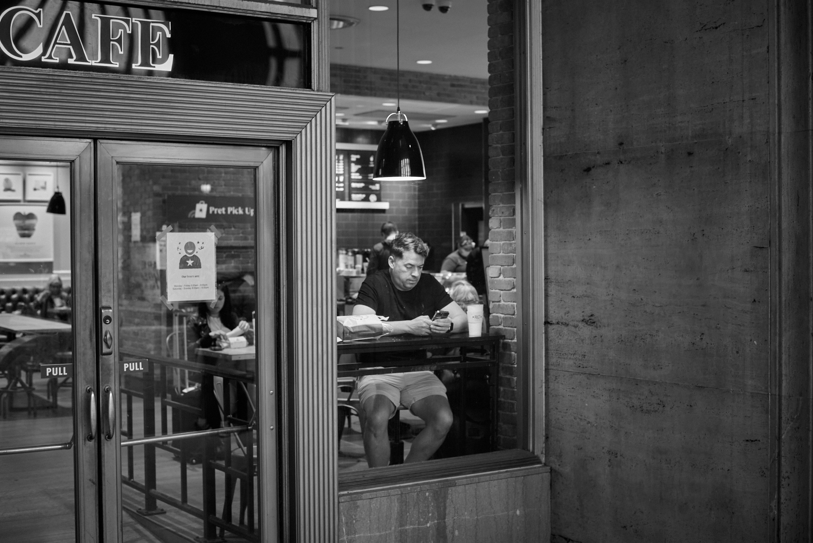 Urban #230510.4. A black and white photo of a man sitting in Pret à Manger in 30th Street Station looking at her phone.