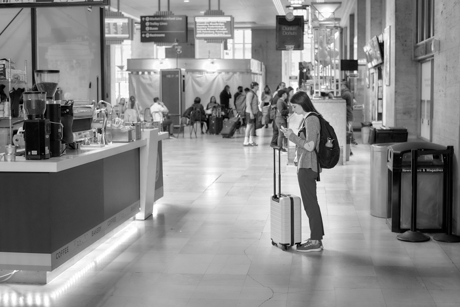 Urban #230510.5. A black and white photo of a woman standing in 30th Street Station looking at her phone.