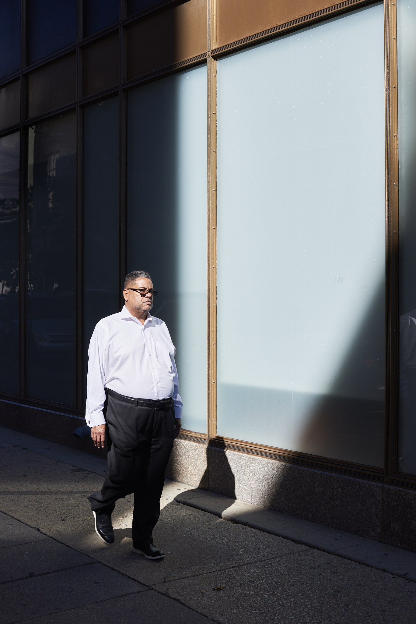 Urban #231013.2. Color photograph of a man strolling into a sunny space, surrounded by shadow.