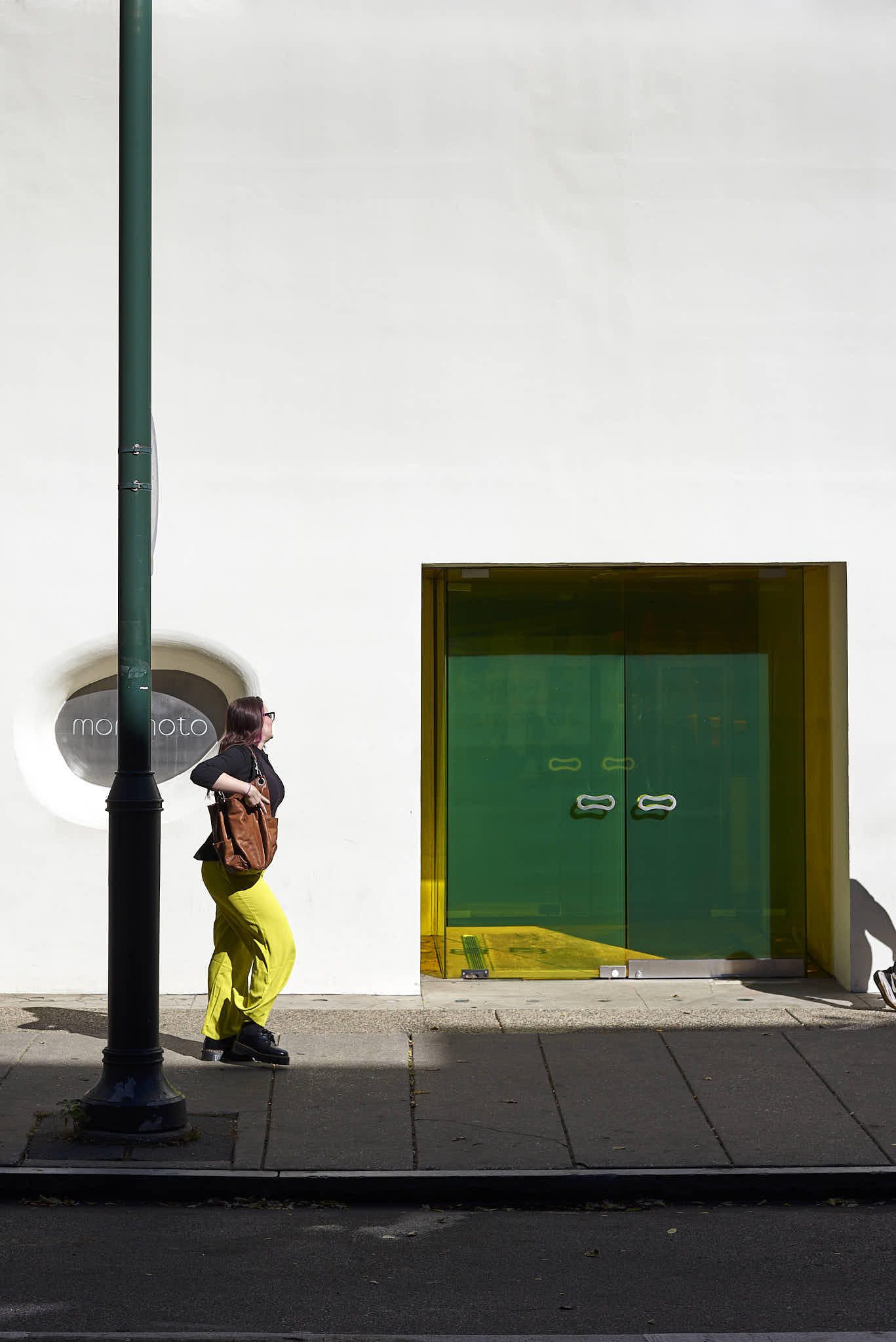 Urban #231013.3. Color photograph of a woman walking along a sidewalk in front of a white wall.