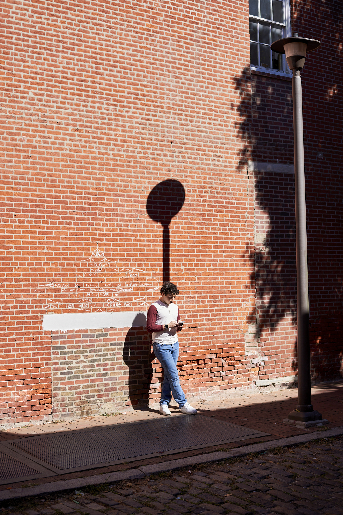 Urban #231013.8. Color photograph of a man leaning against a wall, looking at his phone.