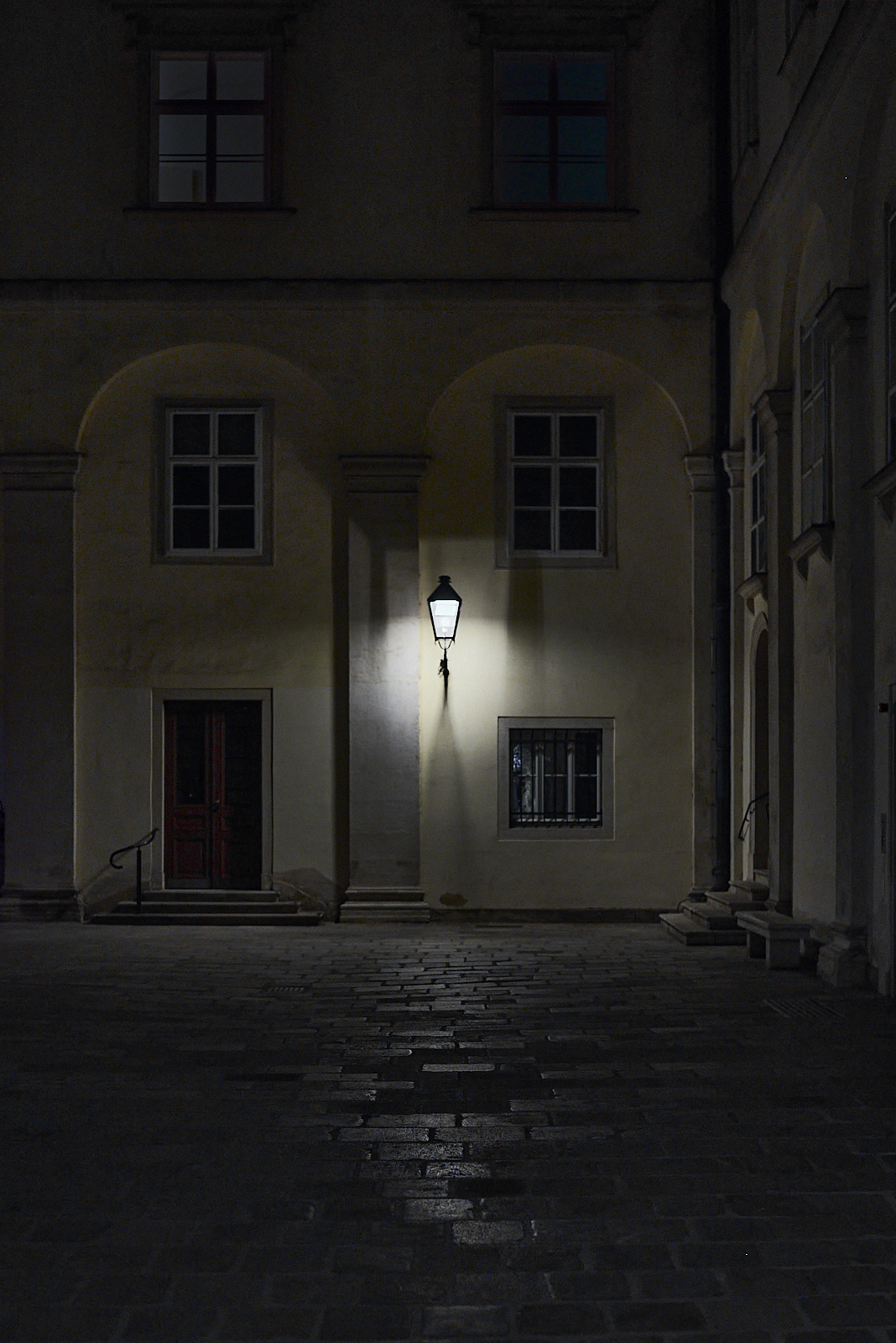 Urban #240309.1. A dark photograph of a corner of a courtyard, one light and a door.