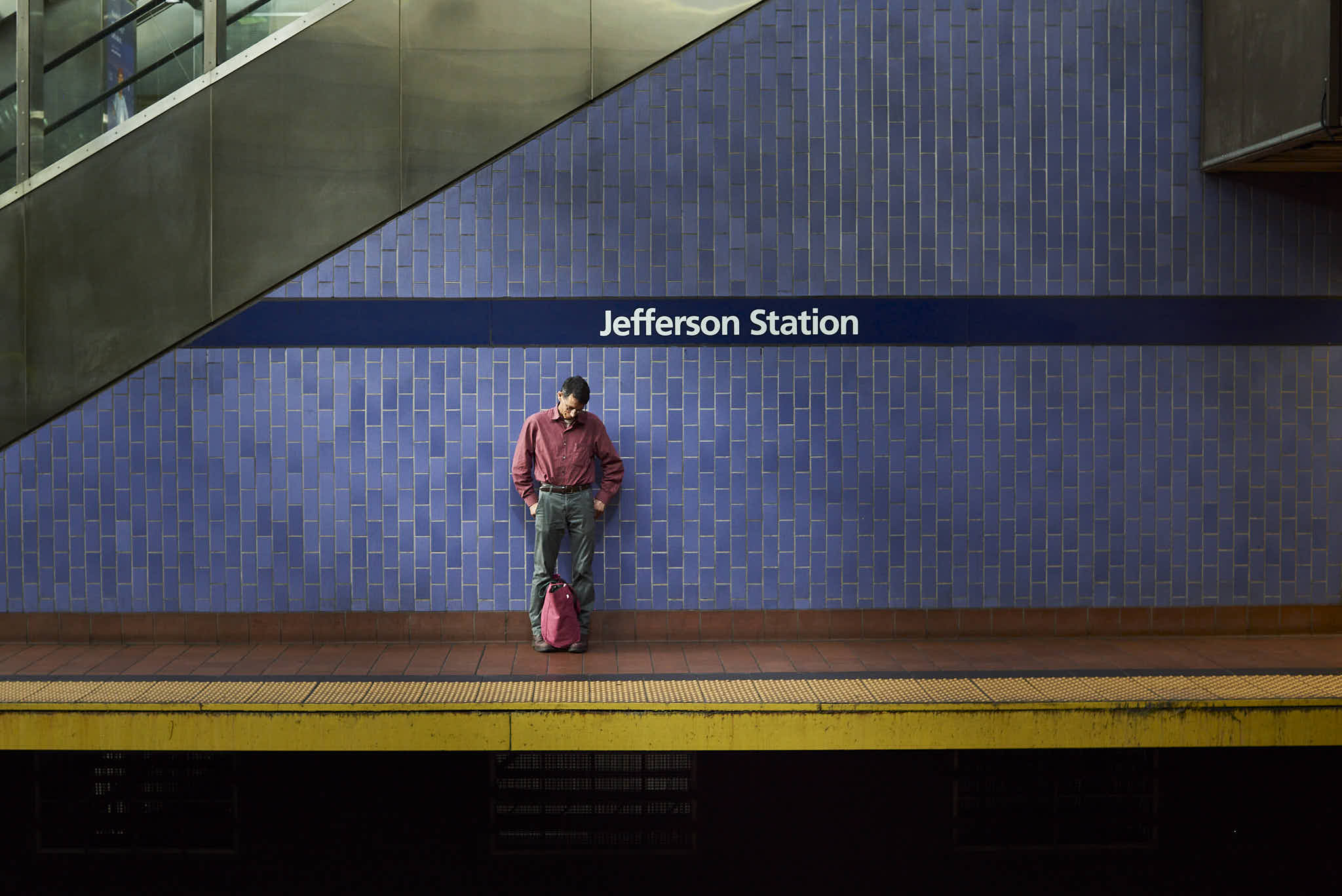 Man standing along a blue tiled wall. On the wall are the words Jefferson Station.