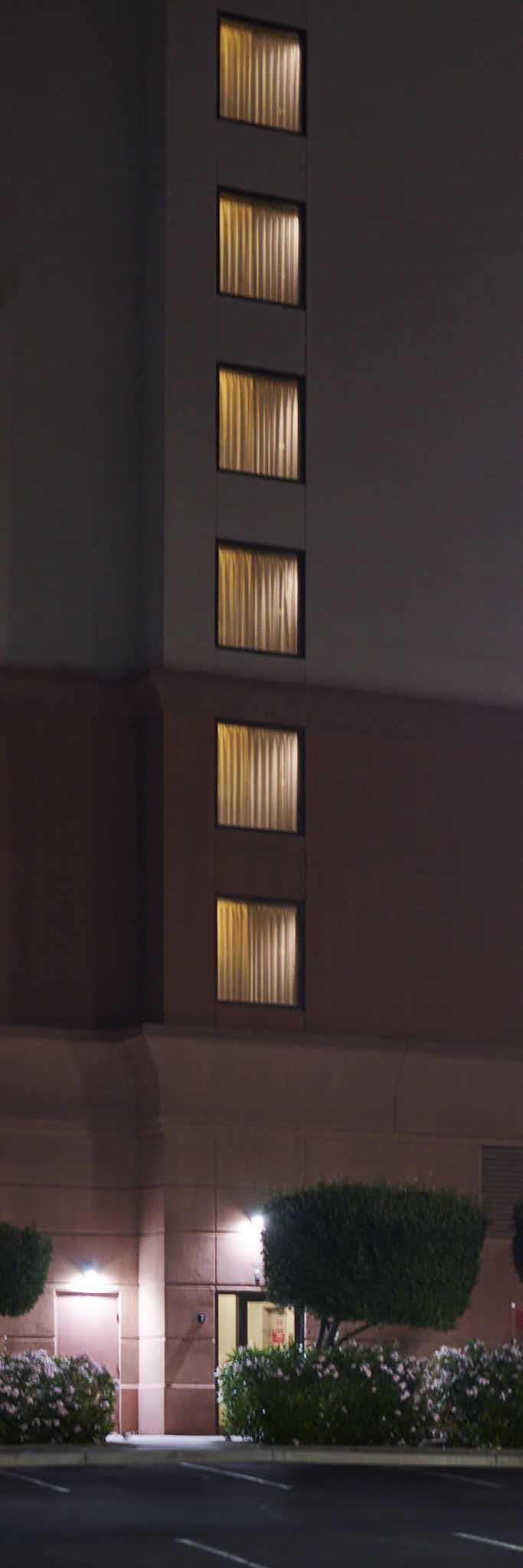 Urban #250417.0. A color picture of a column of windows at night. Lights inside the windows illuminate the curtains.