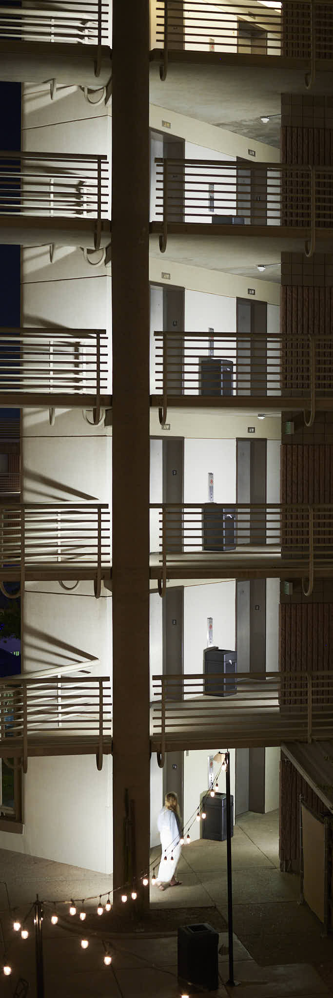 Urban #250417.1. A color photo of a six floors at a hotel, at night. A woman can be seen on the ground floor.